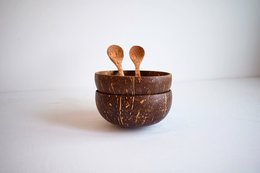 Two coconut bowls with wooden spoons, filled with fresh strawberries, nuts, and herbs.