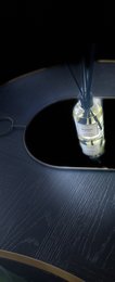 A modern, black scent diffuser with a glass vessel and a feather-like diffuser. The diffuser is designed to disperse fragrance throughout a room.