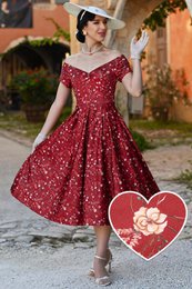 A red off-shoulder dress with a dainty floral print, suitable for women. The dress has a fitted bodice and a flared, knee-length skirt. The dress is available in sizes 8 to 26.