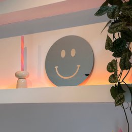 Large round wall mirror with a smiley face design, made of cream-colored material. Suitable for home decor and adding a cheerful touch to any room.