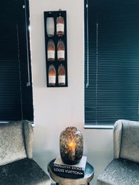 A wooden wine display rack that can hold 6 bottles of wine. The rack has a rustic, farmhouse-style design with a dark finish. It is mounted on the wall and features individual compartments for each bottle.