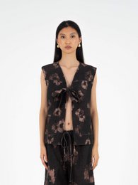 A sleeveless denim vest with a floral print pattern in shades of pink and black. The vest has a V-neckline and a relaxed, oversized fit.