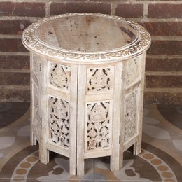 A round, white side table made of mango wood with intricate carved patterns on the sides.