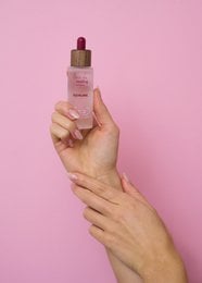 A clear, glass bottle with a red cap containing a squalane facial oil product. The bottle is placed on a wooden surface.