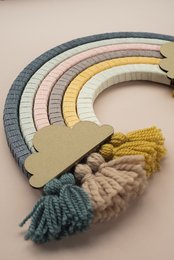 Colorful, handmade rainbow-shaped wall hanging with tassels and wooden shapes in various pastel shades.