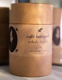 Whole coffee beans in a brown paper package labeled "CAFÉ INTÉGRAL 50G". The beans appear to be roasted and have a rich, dark color.