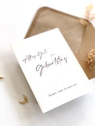 Elegant birthday card with envelope in nude color. Handwritten calligraphic text "Happy Birthday" on the card.