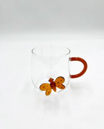  A clear glass mug with a colorful butterfly design on the side. The mug has a red handle and appears to be made of high-quality materials.