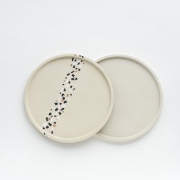 Beige round trinket tray with terrazzo vein pattern and black speckles.