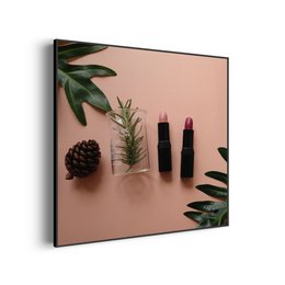 A square painting featuring a minimalist still life composition of makeup products and natural elements against a pink background. The image includes lipsticks, a pine cone, and lush green leaves, creating a visually appealing and stylish aesthetic.