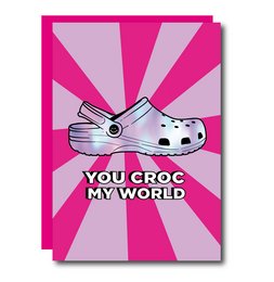 "A pink and purple greeting card with a graphic of a Croc shoe and the text 'You Croc My World'."

The image shows a pink and purple greeting card with a graphic of a Croc shoe and the text "You Croc My World" printed on it. The card appears to be part of a collection or display of similar cards. Based on the product title and category, this card is likely part of a line of greeting cards with text-based designs.