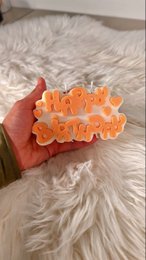 Vibrant orange birthday candles in the shape of the word "HAPPY" on a soft, fluffy white background.