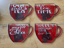 Red ceramic coasters with text "You're my cup of tea" and "There's always time for tea" in white text. The coasters have a heart-shaped design and appear to be for holding tea cups or mugs.