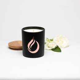 A tall, round black soy candle with a pink flame logo. The candle has a floral, aromatic scent.