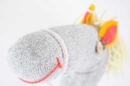  A gray plush toy horse with colorful mane and tail. The toy has a soft, textured body and appears to be made of knitted or crocheted material.
