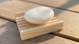 Wooden soap dish with a white soap bar on a wooden surface.