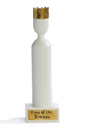 A white ceramic candle with a gold crown-shaped top, labeled "King of the kitchen". The candle appears to be a decorative home accent piece.