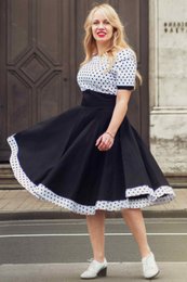  A retro-style swing dress in a white and black polka dot pattern, with a fitted bodice and a full, flared skirt. The dress has short sleeves and a classic, feminine silhouette.