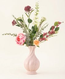 Vibrant bouquet of pink roses, greenery, and other colorful flowers in a white ceramic vase.