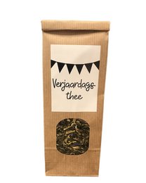 A festive birthday tea in a brown paper bag with a black and white bunting design. The tea leaves are visible through the bag.