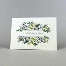 Postcard with a floral design featuring various plants and greenery on a textured paper background.