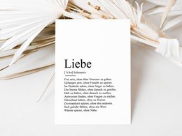 A white postcard with the German word "Liebe" (meaning "love") printed on it, surrounded by open books and feathers.