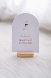 A wine glass icon on a white card with the text "Bedankt voor de wijn dan" which means "Thank you for the wine then" in Dutch. The card has a simple and elegant design, suitable for a Christmas card or a thank you note.