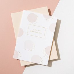 A vellum pink envelope with a "Birthday Girl" card. The card features a minimalist design with a white background and subtle pastel shapes.
