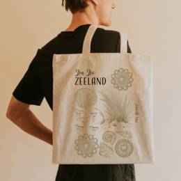 Beige tote bag with "Zon Zee Zeeland" text and floral design, suitable for shopping or everyday use.