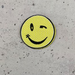 'Smile iron-on patch with a cheerful yellow smiley face design. The patch can be easily applied to clothing, bags, or other fabric items.'