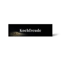 Black rectangular sticker label with "Kochfreude" text and gold spice particles design