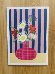 Colorful striped vase with vibrant flowers, including daisies and other blooms, on a patterned background.