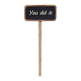  A small chalkboard sign on a wooden stick that says "You did it", displayed in a hand holding a potted plant.