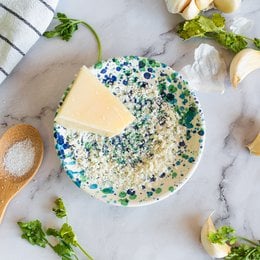 A round, multicolored grater with a speckled pattern of green, blue, and white. The grater appears to be made of ceramic or porcelain material.