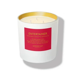 White cylindrical scented candle with gold lid, red label, entertainer fragrance, luxury home decor.