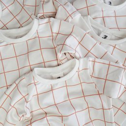A white sweater with an orange grid pattern. The sweater has a crew neck and appears to be made of a soft, cozy material. It is suitable for children and would be a stylish and comfortable option for casual wear.