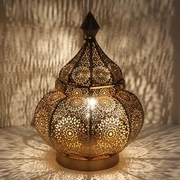 Ornate gold-colored table lamp with intricate floral pattern that casts a warm, ambient light.