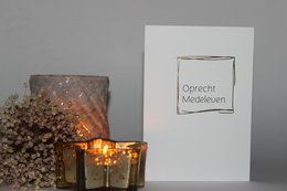 A simple, elegant greeting card with the text "Heaven Sincere condolences" printed on a white card. The card is accompanied by decorative glass candle holders with flickering flames, creating a somber and reflective atmosphere.