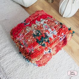 A round, plush Moroccan-style pouf in shades of pink and beige with a geometric pattern, suitable for use as an ottoman or extra seating.