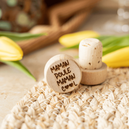 A cork and wood wine bottle stopper with the text "Maman Poule, Maman Cool" printed on it. The stopper has a natural, rustic appearance and is surrounded by lemon slices and other kitchen ingredients.