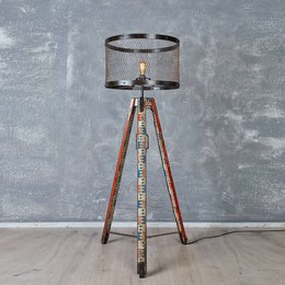 A tall, tripod-style floor lamp with a cylindrical shade and a wooden base. The lamp has a warm, rustic aesthetic.