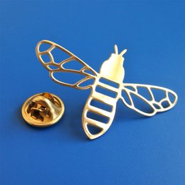 A gold-colored brooch in the shape of a bee with intricate wing details against a bright blue background.