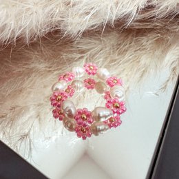 A delicate glass bead ring in a floral design, featuring a rose-colored pearl centerpiece. The ring has a feminine, elegant style.