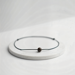 A simple, minimalist bracelet with a single black bead on a thin black cord.