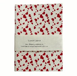 A5 notebook with a soft cover, eco-friendly paper, and a heart print pattern in red on a light background. The notebook is handmade in Nepal.