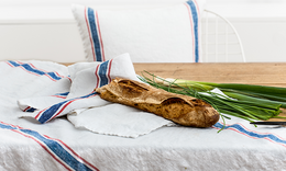 Linen table runner in a striped pattern with green onions and a wooden board.
