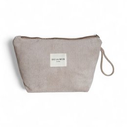 A large, beige makeup pouch with a ribbed texture and a label that says "De La Mer" on it.