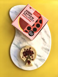 Aged cashew-based cheese with pink peppercorns, served on a plate with asparagus.
