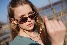 Gold-toned chain with black accents, suitable for holding sunglasses or eyeglasses. Stylish accessory for fashion-forward individuals.