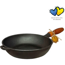 A large, round cast iron frying pan with a wooden handle. The pan is black in color and suitable for use on all heat sources. It is PFAS-free.